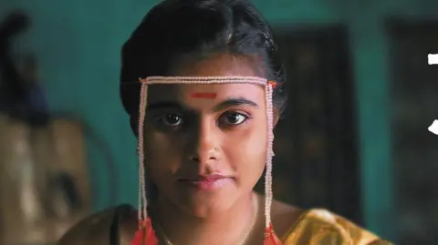 Courtesy: Sthal A Still From Sthal: Pertandingan menunjukkan karakter utama yang dimainkan oleh Nandini Chikte duduk di bangku kayu 