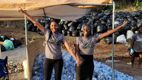 Atas perkenan manusia yang baik 268 Kelisha dan Joshuanette berpose untuk foto di depan tumpukan botol plastik yang telah mereka kumpulkan untuk didaur ulang