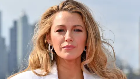 Getty Images Blake Lively dalam setelan jas putih dan anting-anting berpose di depan cakrawala London pada 8 Agustus