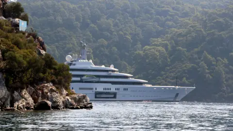 Getty menggambar gerhana super-yacht, muncul dari balik singkapan berbatu di Mediterania dekat Turki, dengan lereng bukit berhutan di belakangnya. Sebuah pintu di sisi kapal pesiar terbuka untuk mengungkapkan kapal yang lebih kecil di dalamnya