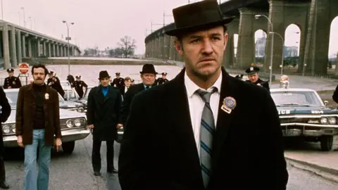 Getty Images Gene Hackman di The French Connection, mengenakan mantel dan topi hitam