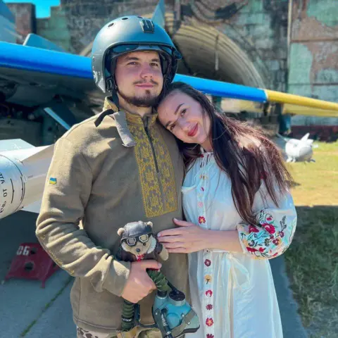 Maria Smerechanska Ivan, seorang pria Ukraina berusia 31 tahun yang mengenakan helm, berdiri di depan pesawat bersama istrinya Maria, 29