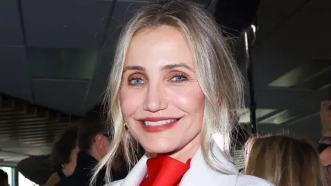 Getty Images Cameron Diaz di Stella McCartney Fashion Show baru -baru ini. Dia memiliki rambut pirang tersapu dan mengenakan blus merah dan jaket putih.