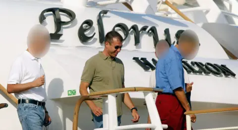 Roman Abramovich, mengenakan kacamata hitam, celana jeans dan kemeja polo khaki, melangkah dari geladak pelorus dengan beberapa rekan, dengan nama kapal pesiar terlihat di belakangnya