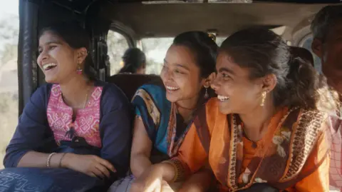 Courtesy: Sthal A Still From the Marathi Film Sthal: A Match menunjukkan tiga wanita muda yang tertawa. Karakter utama yang dimainkan oleh Nandini Chikte ada di sebelah kanan